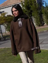 Buzo color crudo con cuello de piel sintética color crema, abertura parcial con cierre de cuero marrón y hebilla dorada, puños con ajuste de cuero marrón y bolsillos laterales.