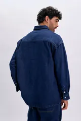 Sobrecamisa de jean color azul oscuro, de corte oversize, con mangas largas, bolsillos frontales con solapa y cierre con broches a presión.