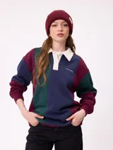 Sweater estilo rugby de Rusty, con diseño color block en tonos bordó, azul marino y verde. Presenta cuello polo en color crema con cierre frontal de botones, mangas largas con puños elásticos y logo de la marca bordado en el pecho.