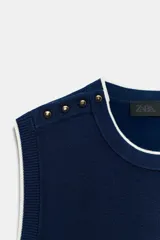 Jersey de punto azul marino sin mangas, con cuello redondo, ribetes en contraste y detalles de botones dorados en el hombro.