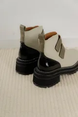 Borcego de cuero color marrón con suela track negra de goma. Presenta un diseño de caña corta con cierre mediante dos tiras de velcro en el empeine y costuras decorativas a la vista.