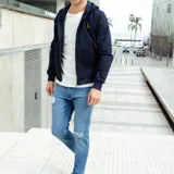 Campera azul marino de gabardina con capucha, cierre frontal con cremallera, puños y cintura acanalados y un pequeño logo bordado en el pecho.