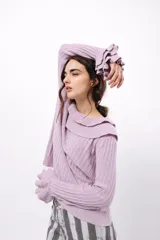 Buzo de tejido acanalado color lila, con cuello redondo decorado con dos volados y mangas largas con tres volados pequeños en los puños.