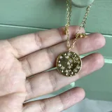 Collar de cadena fina dorada con dije principal circular con relieve y cristales incrustados, acompañado de dijes colgantes de luna creciente y estrella, también con cristales.