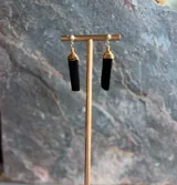 Aros colgantes con piedra natural negra en bruto, envuelta en alambre dorado en la parte superior y cierre de gancho.