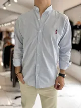 Camisa de manga larga con cuello mao, a rayas verticales celestes y blancas, con pequeño bordado en el pecho.