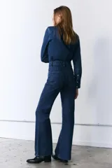 Camisa de denim de corte clásico con cuello solapa, manga larga con puños anchos y cierre frontal con botones. Presenta un diseño de bajo asimétrico.