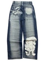 Jean de denim azul de corte regular fit y tiro alto, con efecto desgastado. Presenta estampados en color blanco: un diseño abstracto en el bolsillo trasero izquierdo, una cuadrícula en el bolsillo trasero derecho y un tigre en la parte inferior de la pierna derecha.
