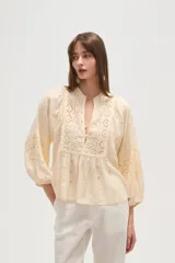Blusa de viscosa color blanco con diseño holgado, cuello en V y cierre frontal con botones. Presenta detalles de bordado tipo broderie en el frente y en las mangas abullonadas.