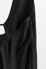 Vestido largo de satén negro, con escote en pico, tirantes finos dobles, abertura en la espalda y bajo asimétrico. Cierre lateral con cremallera oculta.