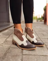 Botinetas estilo western de caña baja, confeccionadas en una combinación de cuero liso y gamuza en tonos marrón oscuro, marrón medio y crema. Presentan cierre lateral, taco bajo cuadrado y diseño con recortes característicos del estilo cowboy.
