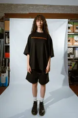 Remera negra de corte holgado con mangas cortas y estampado en color naranja con la frase "Don't believe in my state of cha..."