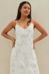 Vestido largo de lino beige con tirantes finos y escote en V, adornado con sutiles bordados florales plateados y lentejuelas.
