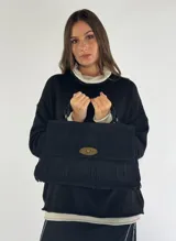 Cartera negra de gamuza con flecos y cierre metálico dorado.