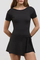 Vestido deportivo corto de color negro, diseñado para pádel. Presenta una estructura superior tipo remera de manga corta con espalda abierta, y una parte inferior que combina una calza corta con una media pollera envolvente que se ata en la cintura. Confeccionado en tejido suave y elástico.