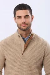 Buzo de punto color beige, con cuello alto y cierre frontal con cremallera y solapa de gamuza con botón. Presenta un tejido texturizado en el cuerpo y mangas lisas.