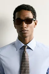 Corbata ancha de seda color marrón oscuro con estampado de raquetas de tenis y volantes. Confeccionada en tejido jacquard con forro de seda.