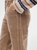 Pantalón de pana roja con corte holgado y tiro medio. Presenta una línea dorada a lo largo de la pierna.