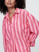 Camisa de corte oversize confeccionada en popelina, con diseño de rayas verticales en tonos verde y blanco. Presenta cuello clásico, cierre frontal con botones y bolsillo en el pecho.