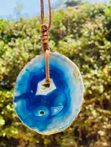 Collar con dije de piedra ágata blanca y marrón, con forma circular irregular y agujero en el centro. El dije está sujeto con un cordón fino de cuero marrón.