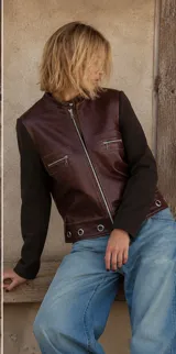Campera de cuero marrón con mangas de lana en color marrón oscuro. Presenta cierre frontal, bolsillos con cierre en el pecho y detalle de ojales metálicos en el ruedo.