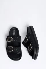 Sandalia plana color negro con dos tiras ajustables mediante hebillas metálicas doradas, decoradas con pequeñas tachas doradas. Cuenta con una suela anatómica y plantilla cómoda.
