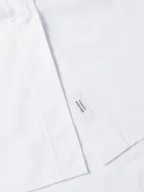 Vestido camisero de corte oversize confeccionado en algodón orgánico. Presenta cuello inglés, cierre frontal de botones, mangas largas con puños abotonados y largo hasta la rodilla. Incluye el logo de la marca bordado en el puño.