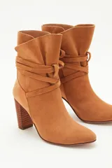 Bota de caña media en gamuzón color suela, con taco cuadrado y tiras envolventes en la caña terminadas en borlas decorativas.