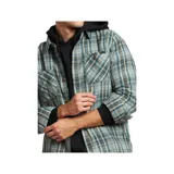 Camisa de manga larga con cuello y botones, con un patrón de cuadros en tonos azules, verdes y marrones. La camisa se lleva abierta sobre una remera con capucha de color claro.