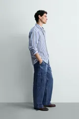 Camisa de corte regular fit confeccionada en tejido de algodón, con diseño de rayas verticales en azul y blanco. Presenta cuello solapa con botones, cierre frontal de botones, manga larga con puños abotonados y un bolsillo en el pecho.