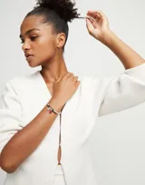 Pulsera Uno de 50 con doble tira, una de cuero marrón y otra de cuentas plateadas. Incluye un dije de corazón plateado y un dije de cristal de Murano rojo.
