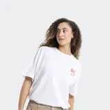 Remera blanca de corte oversized, con cuello redondo y mangas cortas. Presenta un pequeño estampado en el pecho con el logo de la marca Reef en color rojo y detalles de estrellas.