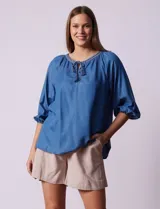 Blusa celeste de tencel con cuello redondo, escote en V y lazo de ajuste. Tiene cuello y escote calado y mangas 3/4 amplias con puño elastizado.