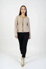 Cardigan de punto color beige con detalle de apliques circulares brillantes en el cuello y a lo largo de la abertura frontal. Presenta mangas largas y un corte recto.