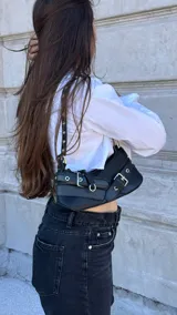 Bolso tipo baguette de cuero sintético negro con múltiples hebillas plateadas.