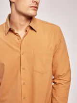 Camisa de franela color tostado, de manga larga, con cuello clásico, cierre frontal con botones y bolsillo en el pecho.