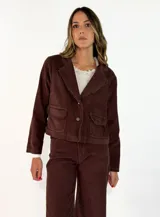 Chaqueta de pana color marrón, con solapas desflecadas, cierre frontal con botones y bolsillos delanteros con solapa desflecada.