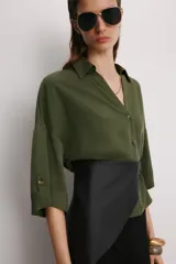 Camisa de corte holgado en color beige, con cuello solapa, escote en pico y mangas cortas amplias. Presenta cierre frontal con botones a tono.