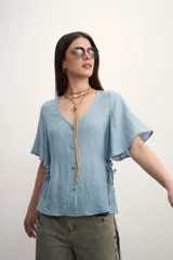 Camisa negra con botones dorados, escote en V y mangas cortas amplias con lazos laterales. 