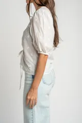 Blusa marrón de algodón con bordados sutiles, escote en V, mangas cortas abullonadas y detalle de fruncido con cordón ajustable en el centro del frente.