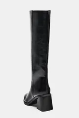 Bota alta de caña media con acabado brillante, tacón cuadrado y punta fina. Diseño minimalista con costura vertical lateral y estilo pull-on.