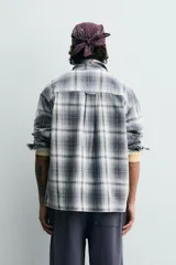 Camisa de algodón de corte relajado, con cuello solapa, manga larga terminada en puño con botón y dos bolsillos de plastrón con solapa en el pecho. Presenta un estampado de cuadros en tonos azules, grises y blancos, y cierre frontal de botonadura.