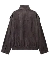 Chaqueta de gamuza en color marrón oscuro, con cuello alto, cierre frontal oculto y bolsillos tipo cargo en el pecho. Presenta un diseño de corte holgado con detalles de charreteras en los hombros.