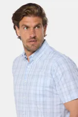 Camisa de manga corta con botones, color celeste con estampado a cuadros blancos. Hecha en Uruguay.