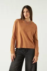 Remera de manga larga color marrón, con cuello redondo y bordado sutil en el pecho izquierdo. Presenta un corte recto con aberturas laterales en el ruedo.