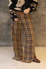 Pantalón de corte oxford con estampado de cuadros en tonos marrones, negros y azules. Presenta un detalle triangular de cuero en la pretina y aberturas laterales en el ruedo.