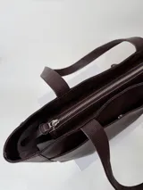 Cartera tipo shopper de cuero marrón texturado, con doble asa de hombro y un bolsillo frontal amplio con cierre de imán.