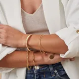 Esclava de alambre redondo en oro 9k, de diseño minimalista, con una medalla colgante que presenta un diseño grabado en forma de estrella con una circonia incrustada.