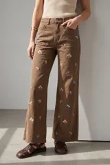 Jean wide leg de tiro alto color marrón, con delicados bordados florales multicolores distribuidos por toda la prenda y dobladillo desmechado.