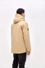 Campera tipo parka de gabardina color beige, con capucha ajustable, cierre frontal y bolsillos laterales con solapa. Presenta un diseño clásico con interior capitoneado.